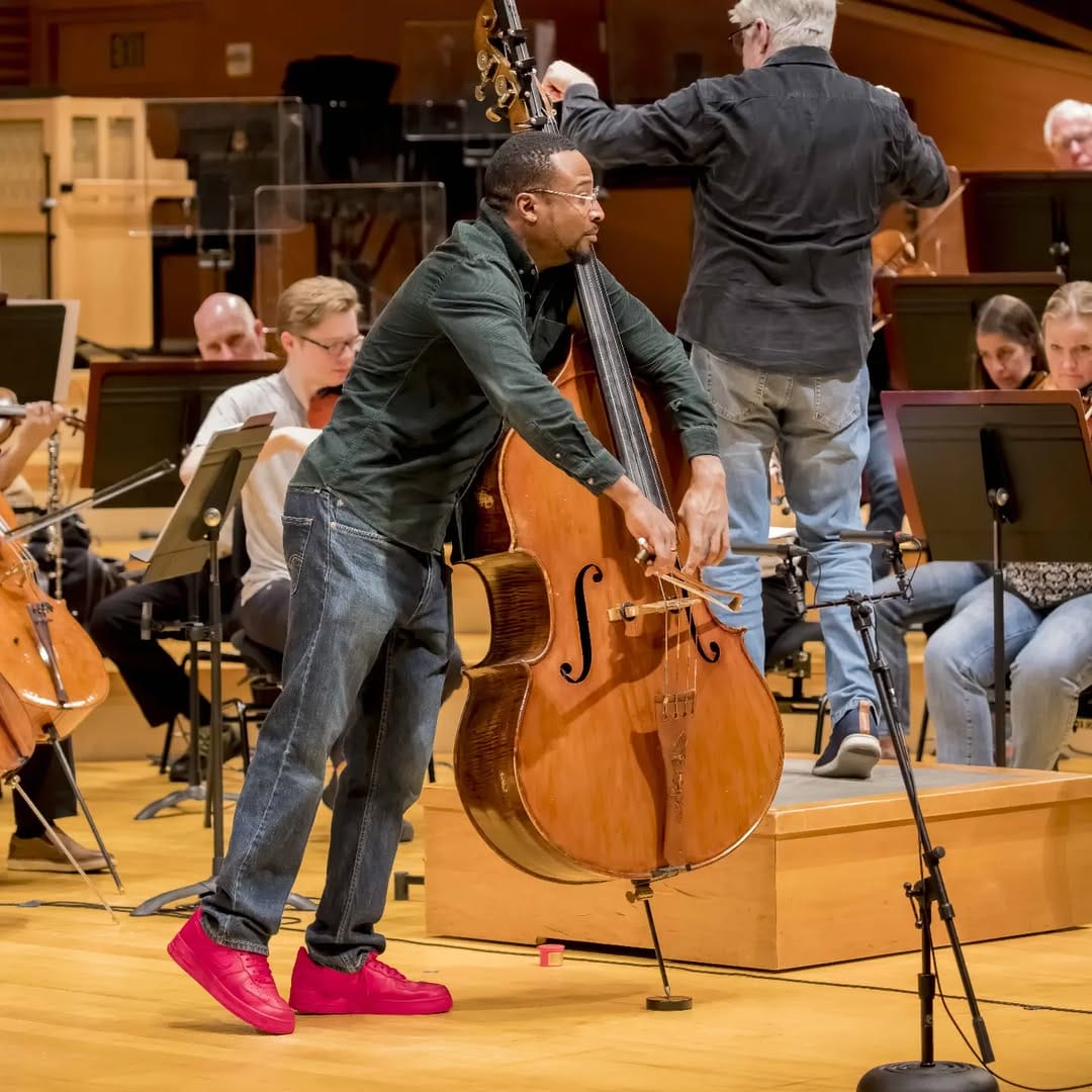 Artist playing the bass in a room with other musicians. 