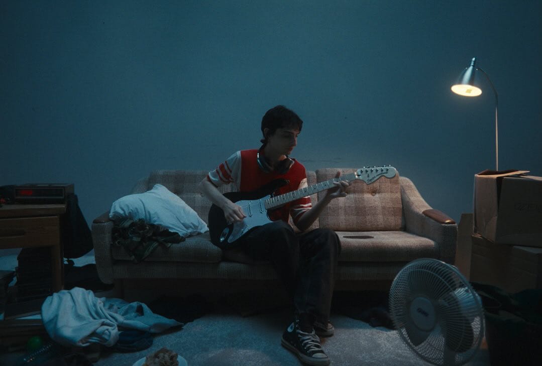 Artist playing guitar on a couch in a low-dimmed room. 