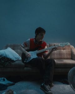 Artist playing guitar on a couch in a low-dimmed room.