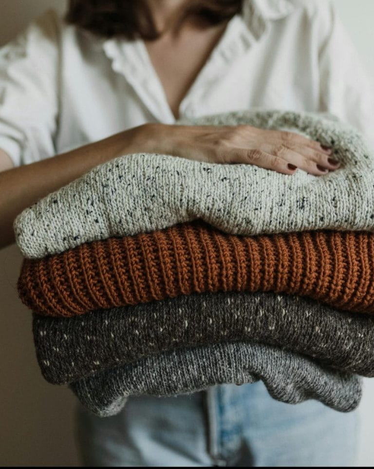 A woman holding a stack of cozy, warm knit sweaters, perfect for winter.
