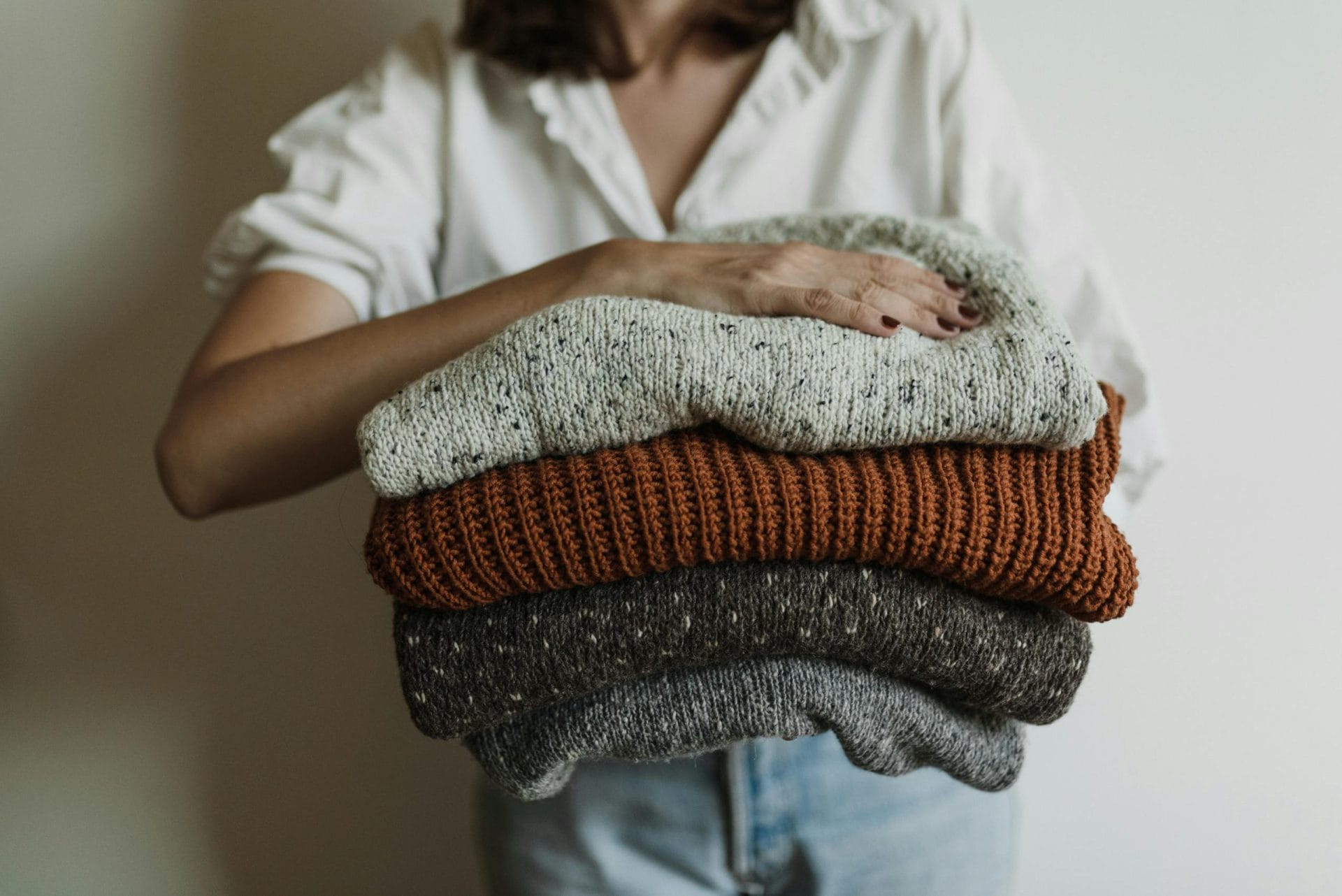 A woman holding a stack of cozy, warm knit sweaters, perfect for wearing in winter in sf.