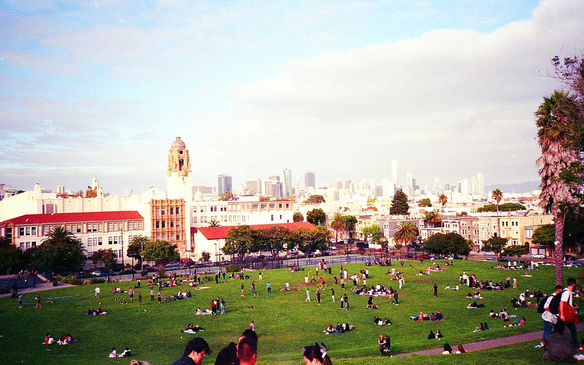 People enjoying a sunny day at Dolores Park with San Francisco skyline views in winters 