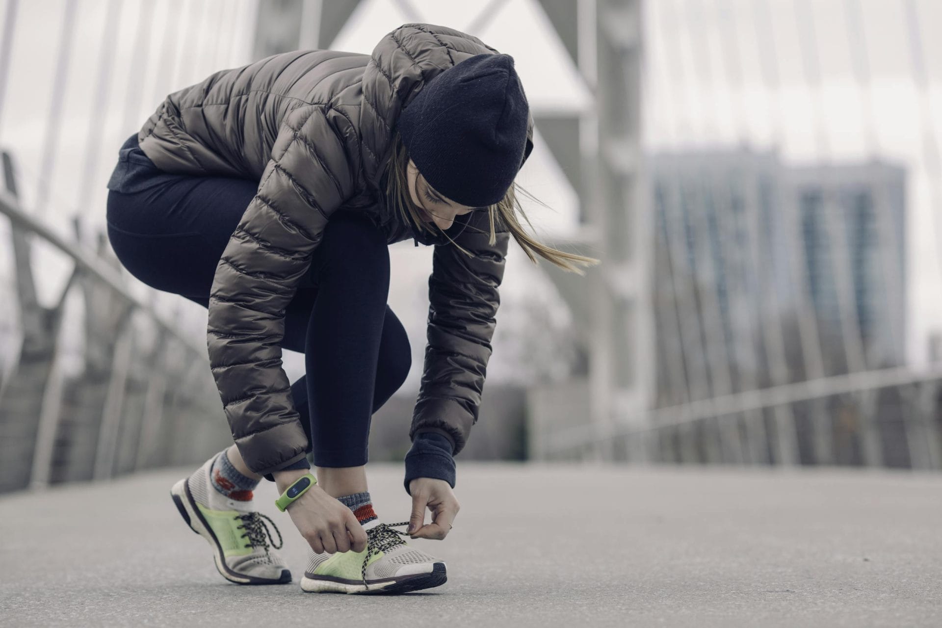 Woman in activewear tying running shoes on a city bridge, ready for a winter jog.