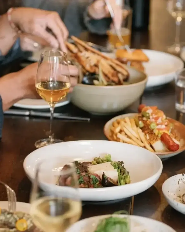 people eating and cutting into food and enjoying wine