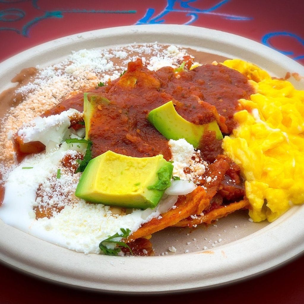 San Francisco Restaurants dish with chilaquiles, red salsa, avocado, cheese, refried beans, and scrambled eggs on a plate.
