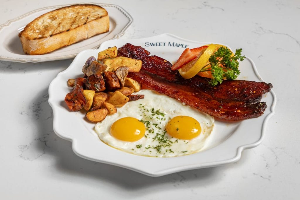 San Francisco Restaurants breakfast plate with eggs, bacon, roasted potatoes, fruit garnish, and toast on a white table.