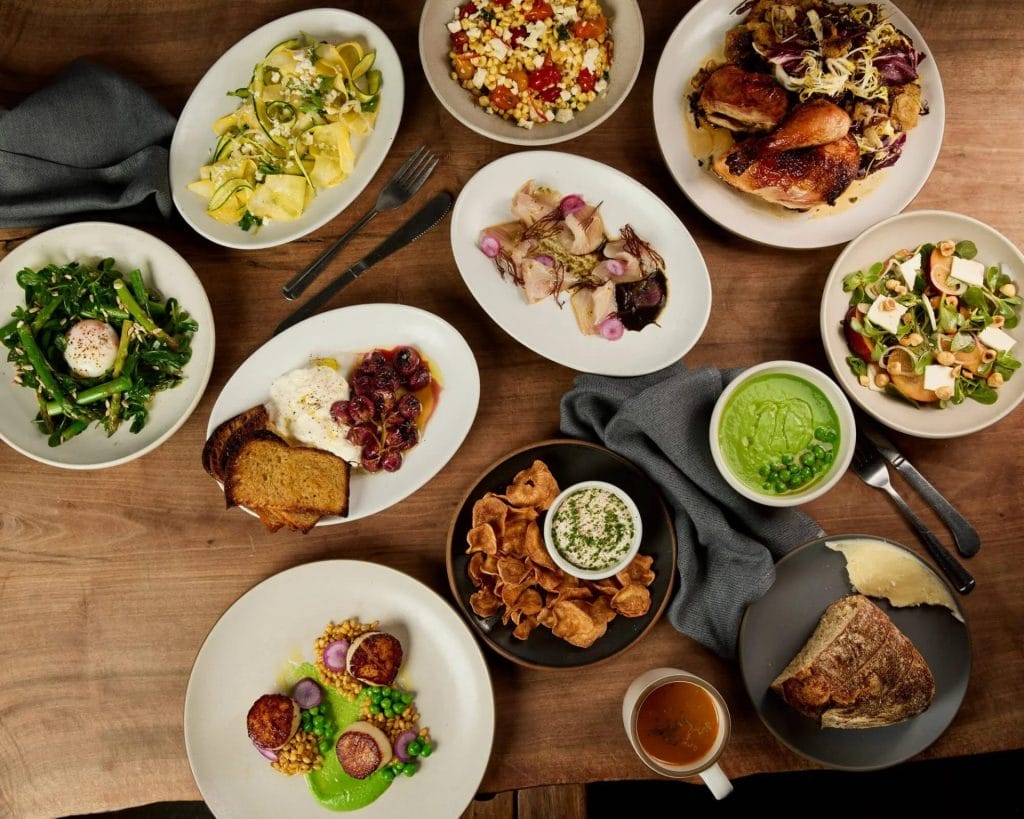 San Francisco Restaurants table spread with roasted chicken, salads, vegetables, bread, dip, and other shared dishes on a wooden table.