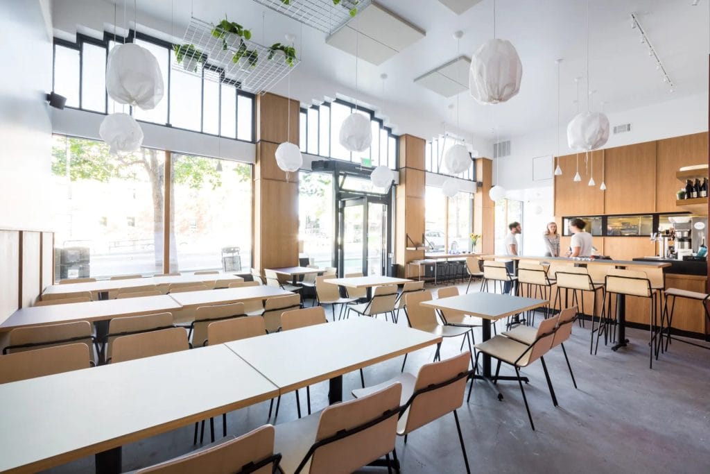 San Francisco Restaurants interior with bright dining tables, hanging lights, large windows, and a counter area in a modern café-style space.