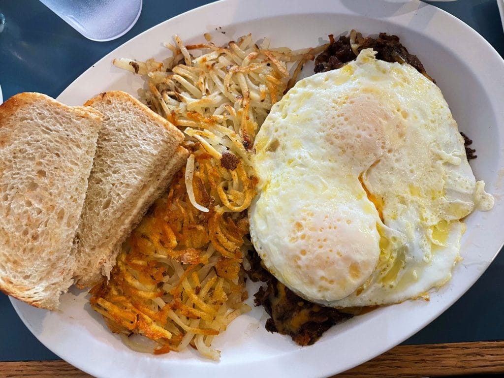San Francisco Restaurants breakfast plate with fried eggs, hash browns, toast, and a side of meat on a white plate.