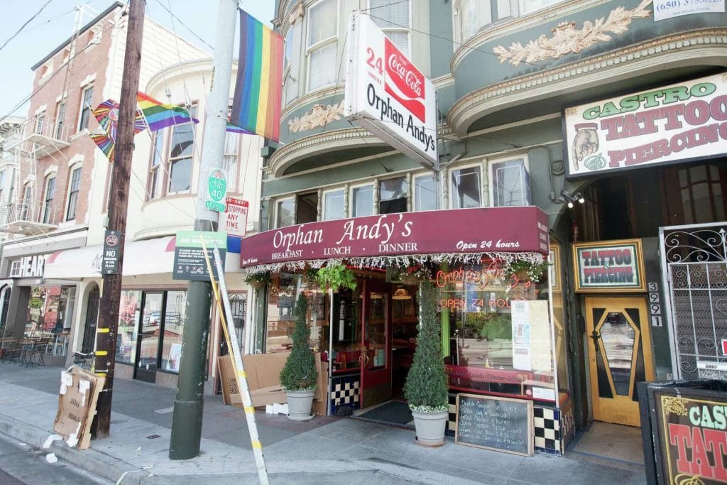 San Francisco Restaurants exterior showing Orphan Andy’s diner with red awning, sidewalk entrance, rainbow flags, and nearby storefronts.