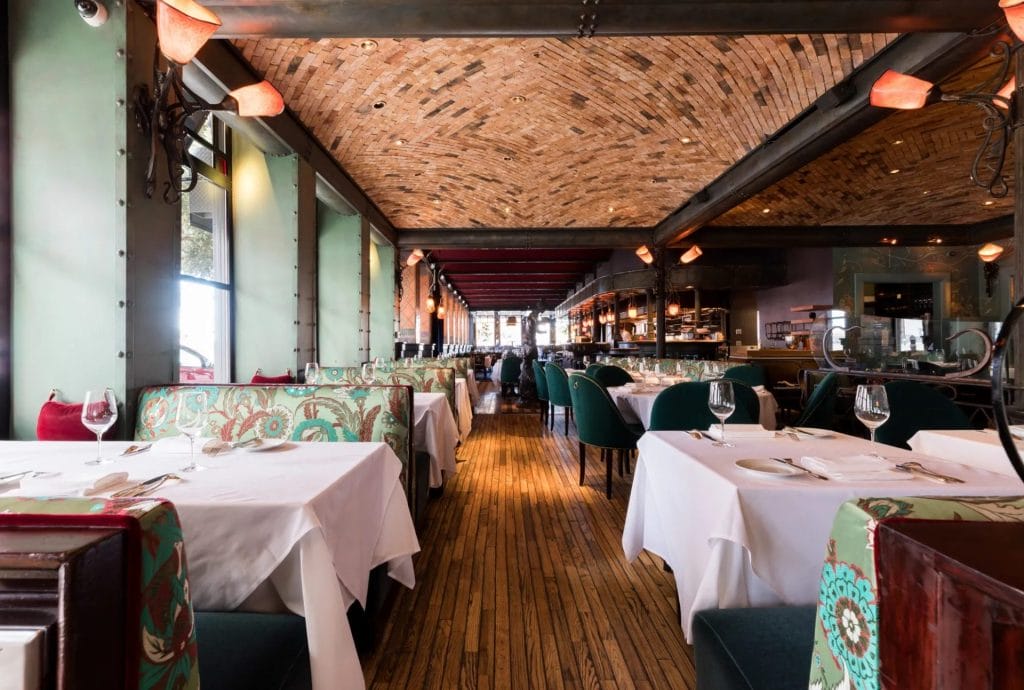 San Francisco Restaurants interior with white tablecloth dining tables, patterned booth seating, wine glasses, and a long wood-floor dining room.
