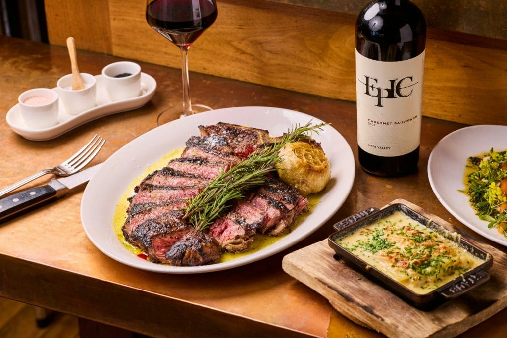 Father’s Day brunch at Epic Steak in San Francisco, featuring sliced steak, roasted garlic, wine, and rich side dishes on a table.