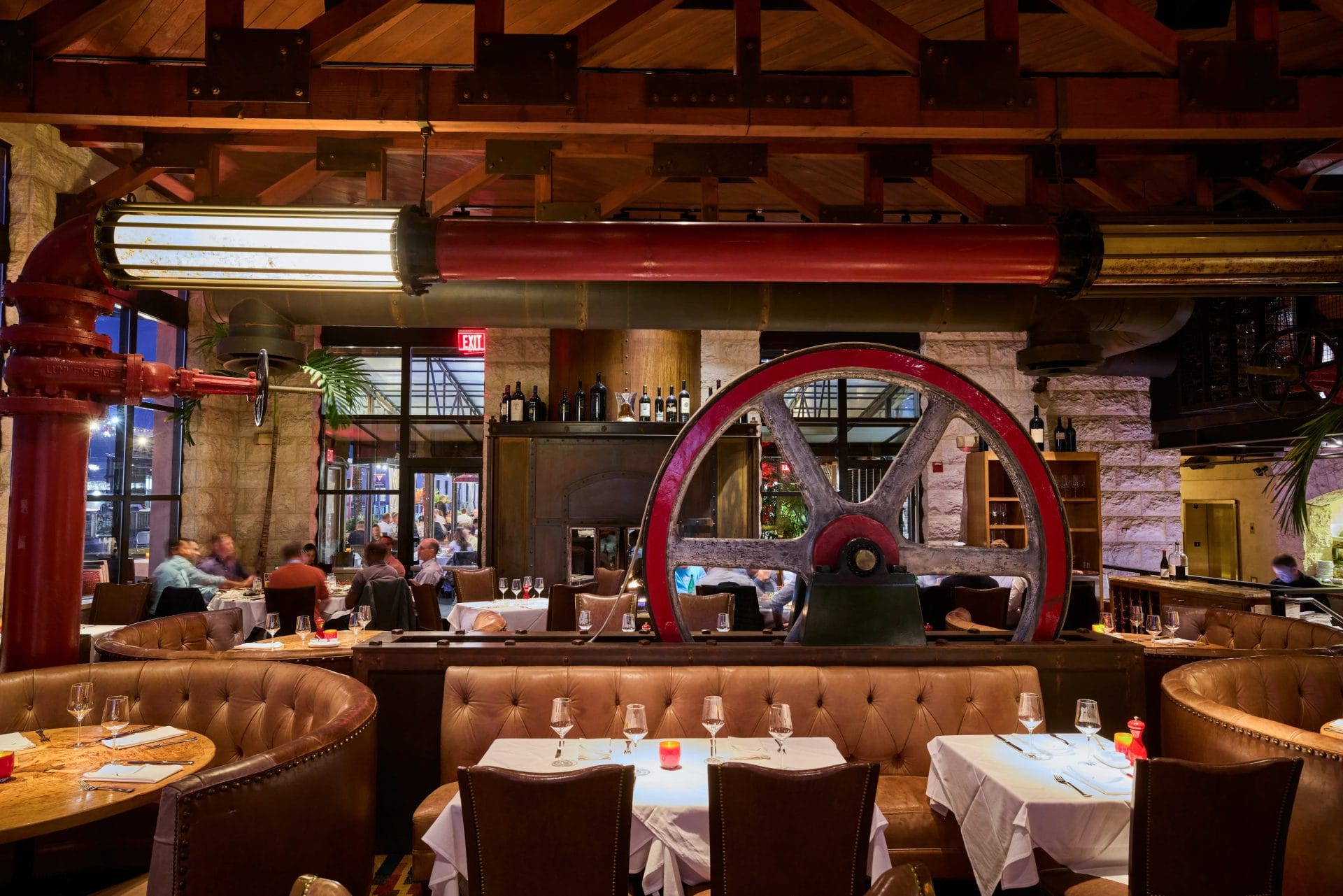 EPIC Steak dining room with leather booths, white tablecloths, industrial decor, and a large red wheel feature in San Francisco.
