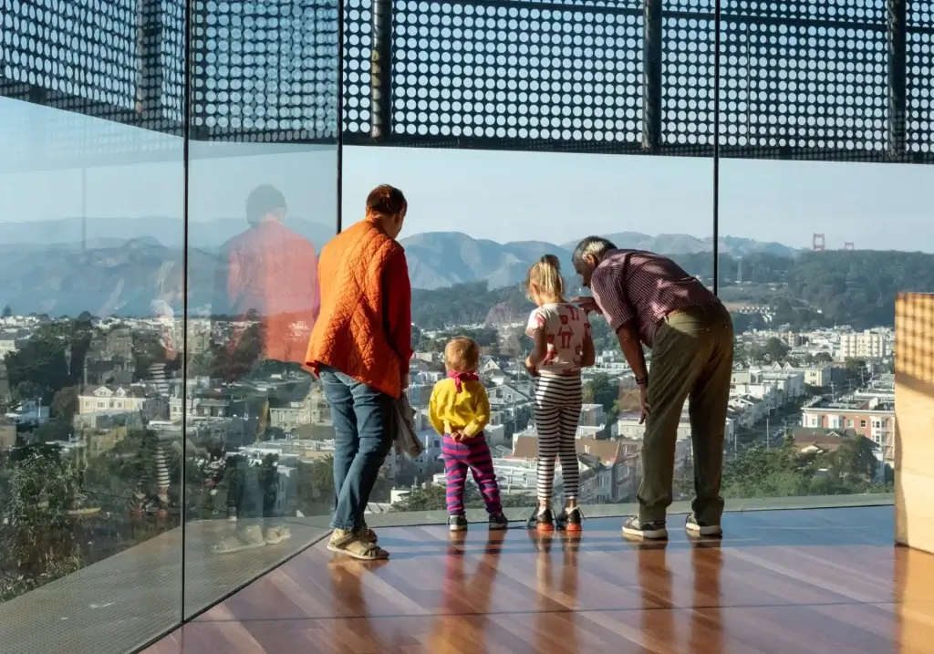 Family looking out over San Francisco from a museum observation window with the Golden Gate Bridge in the distance.