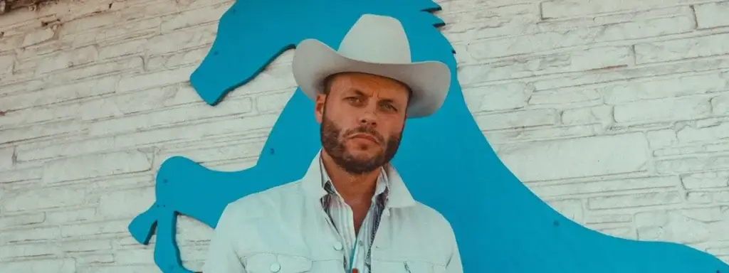 Country music artist in a white cowboy hat standing in front of a blue horse-shaped wall sign.