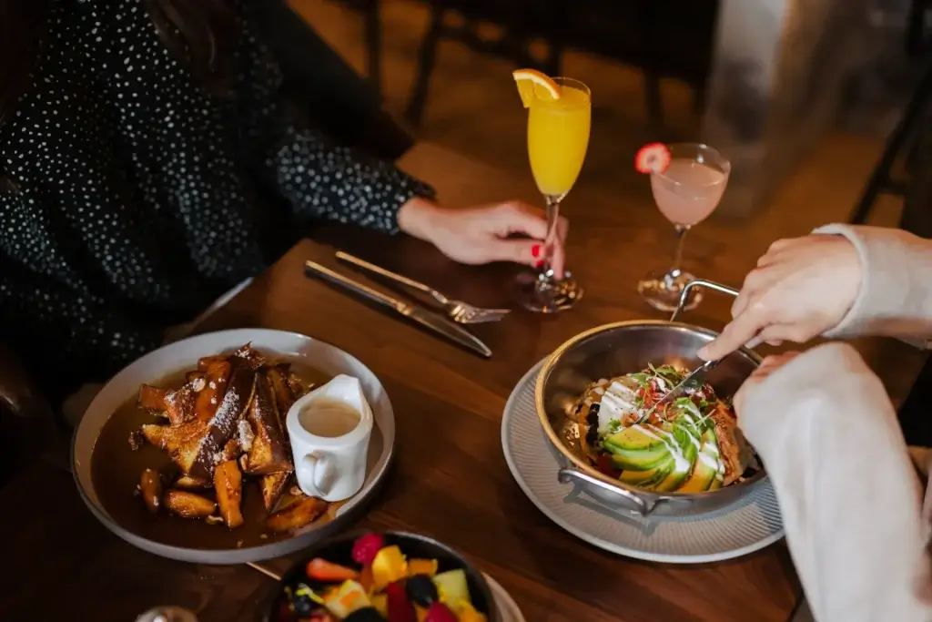 bowl of avocado toast, French toast served with cream and syrup. Orange mimosa and pink cocktail garnished with a strawberry slice.