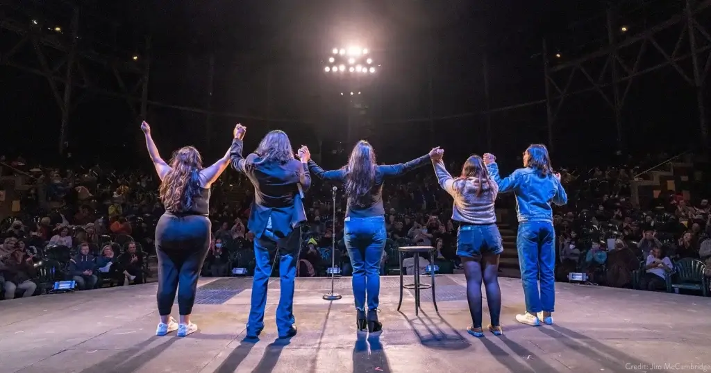 Performers holding hands on stage in front of an audience during a live San Francisco show.