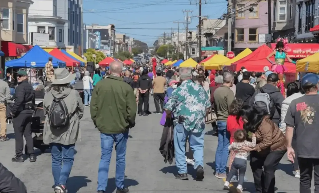 People walking through a San Francisco street festival with colorful vendor tents and outdoor performances.