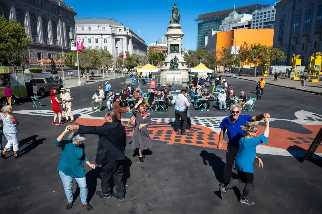 People dancing and sitting at outdoor tables during a Civic Center Soundtrack event in San Francisco.