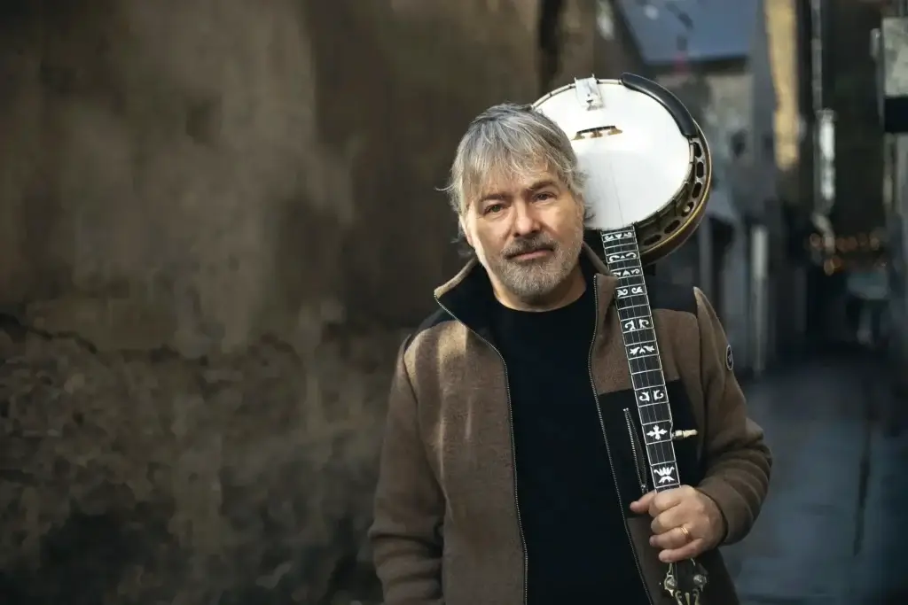 Béla Fleck holding a banjo while standing in a city alley.