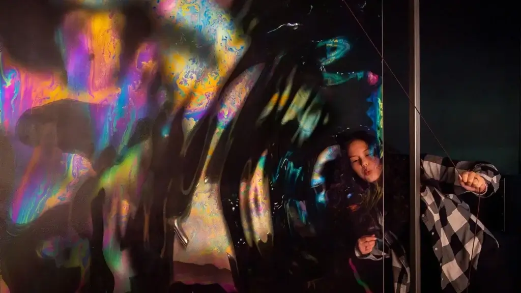 Person creating large soap bubbles with colorful reflections during a hands-on Bay Day activity at the Exploratorium.