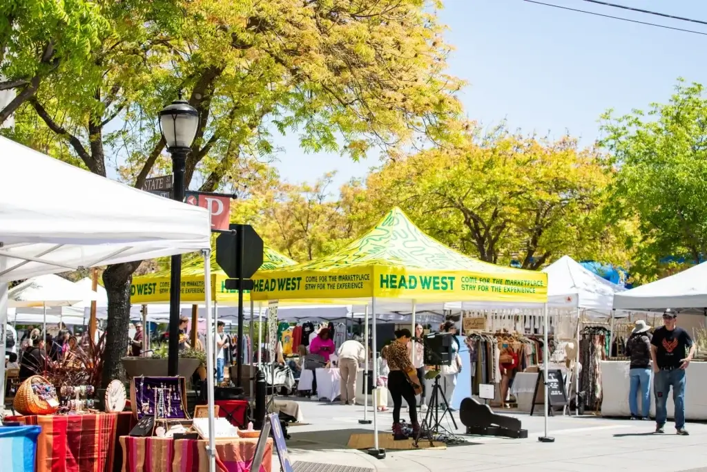 HEAD WEST Marketplace tents with shoppers browsing clothing, jewelry, and local vendor booths outdoors.