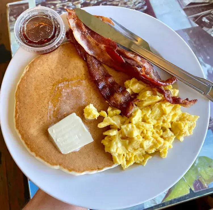 American breakfast, large pancake with a melting butter, bacon strips and scrambled eggs.