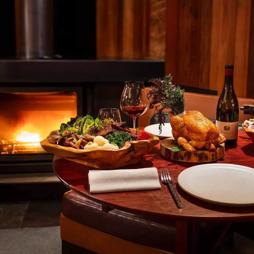 roasted chicken served on a rustic wooden board, a bowl of mixed vegetables and a bottle of red wine