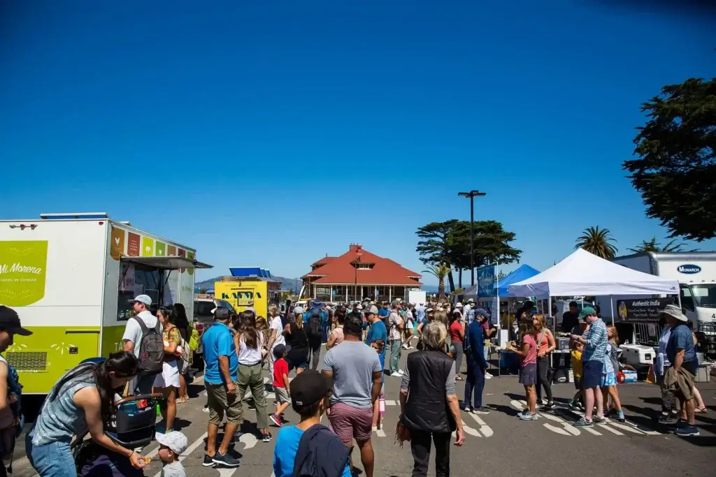 Presidio Pop Up food trucks and vendor tents with crowds gathering outdoors on a sunny day in San Francisco.