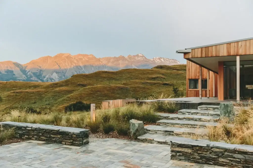 modern wood-clad house with a stone staircase and patio, overlooking green hills and sun-lit mountains in the distance in Point San Luis Lighthouse