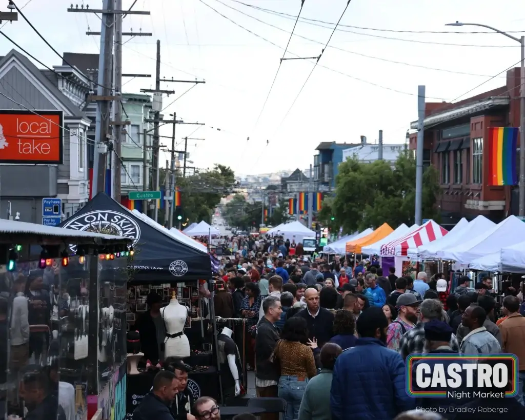 Crowd walking through Castro Night Market with vendor tents, rainbow flags, and neighborhood storefronts.