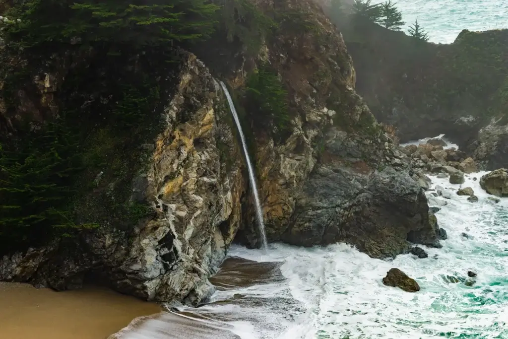 scenic photo of McWay Falls in Big Sur displaying the waterfall cascading from a rocky cliff onto the beach cove with turquoise ocean waves