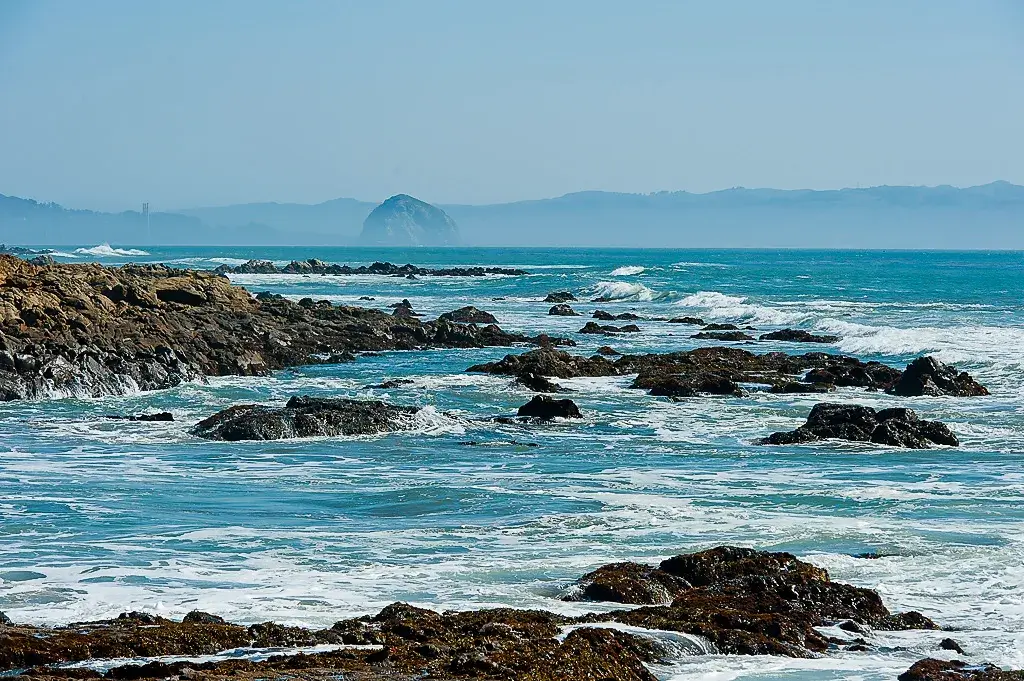 Waves crashing against dark, jagged rocks at Estero Bluffs State Park along the California Coast