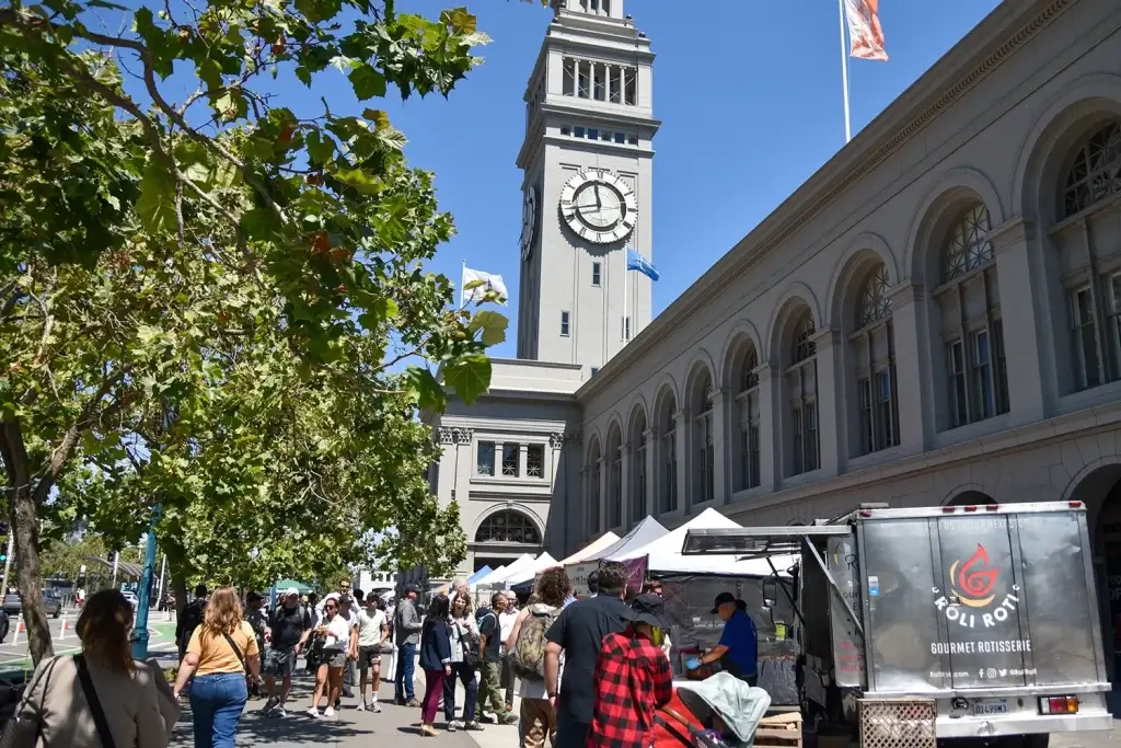 Ferry Plaza Farmers Market outside the Ferry Building with food trucks, vendor tents, and visitors in San Francisco.