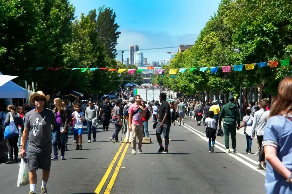 People walking through a car-free San Francisco street during Sunday Streets with colorful banners and trees overhead.